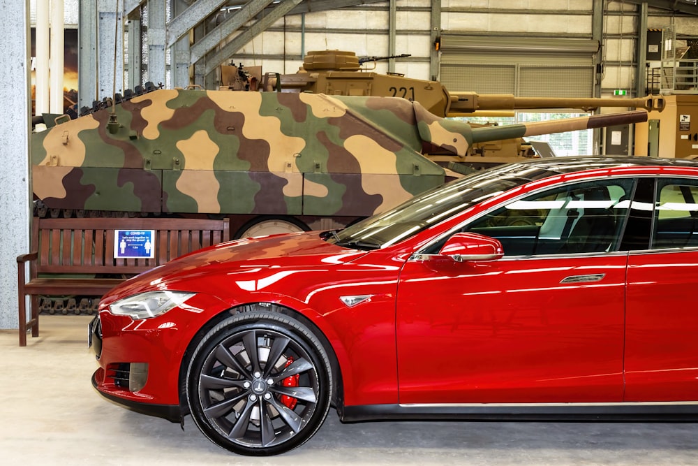 a red car parked in front of a tank