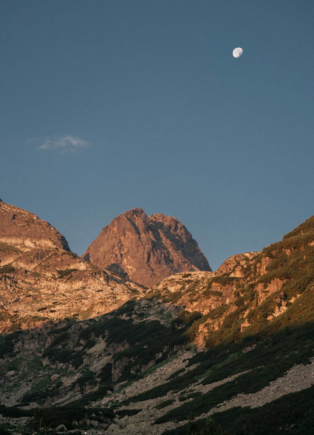 the moon is setting over a mountain range