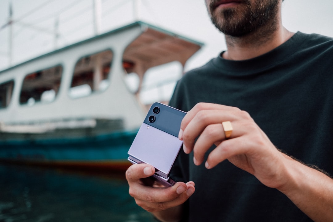 a man holding a cell phone in front of a boat, Young man holding Samsung