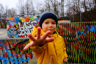 a young boy standing in front of a wall covered in graffiti