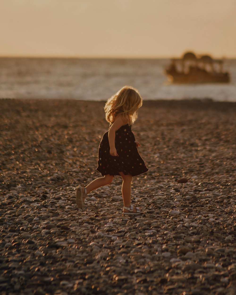 a little girl running on a beach with a boat in the background