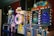 A row of brightly colored arcade game machines is arranged in a line against the wall. Each machine features vibrant lights and designs, with themes ranging from claw games to game show-inspired setups. The area has a playful and inviting atmosphere, suitable for entertainment or amusement centers.