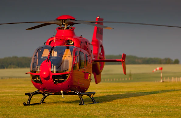a red helicopter sitting on top of a lush green field