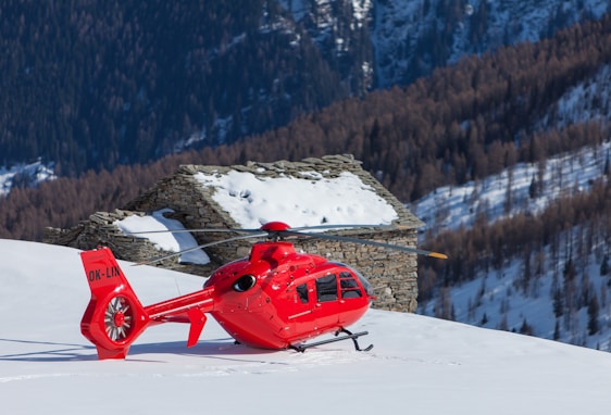 a red helicopter sitting on top of a snow covered slope