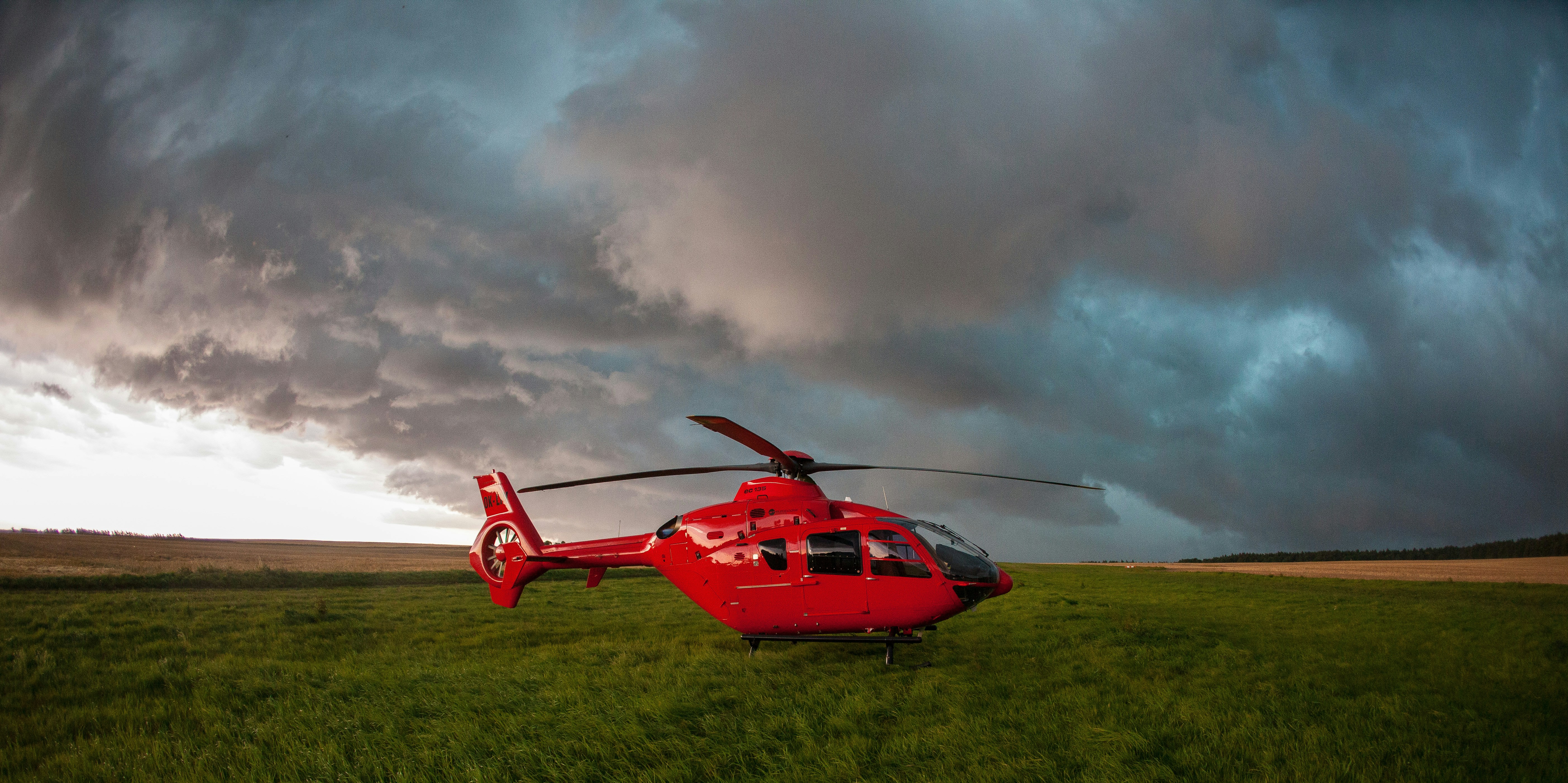 a red helicopter sitting on top of a lush green field, 