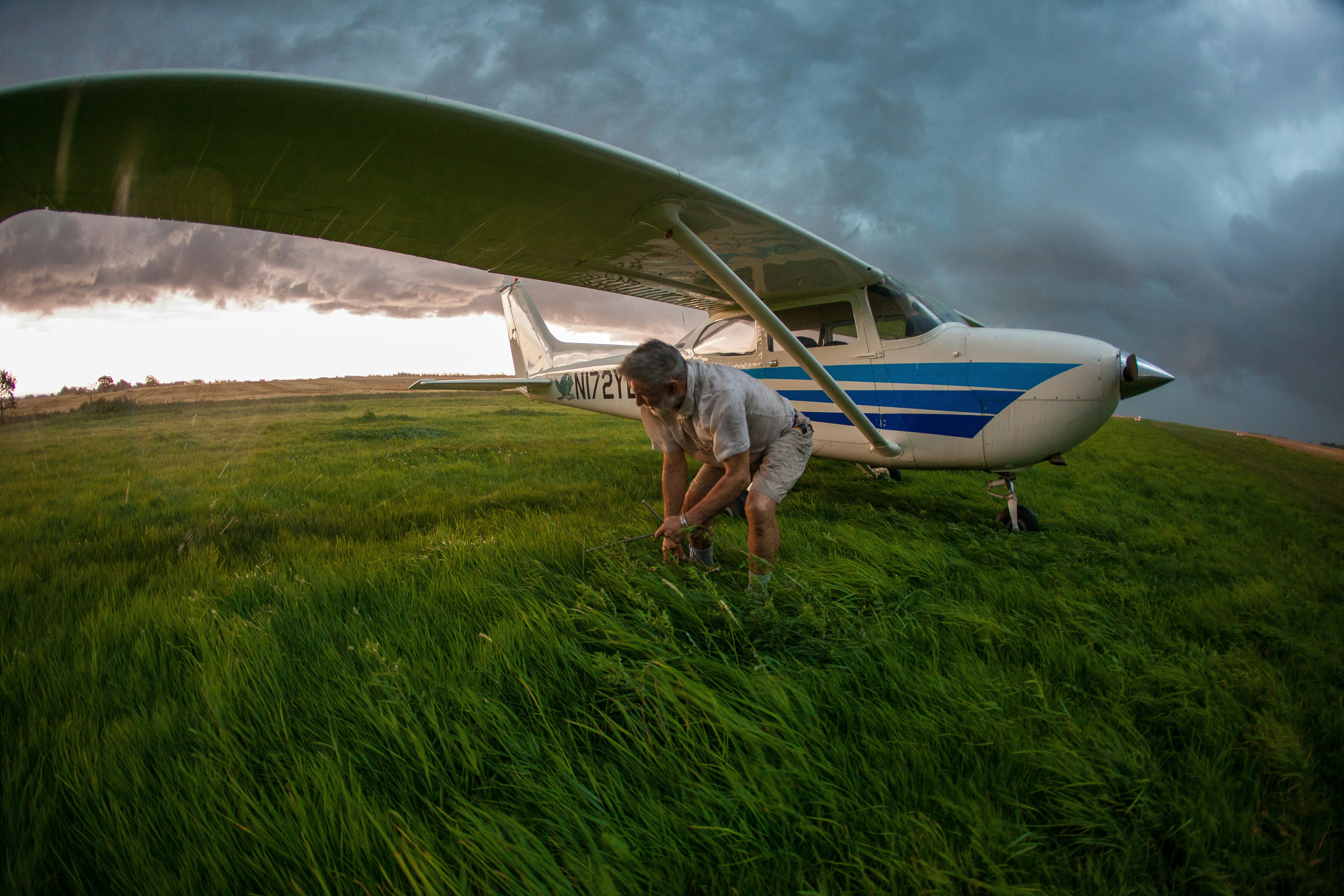 a man standing next to an airplane on a lush green field, 