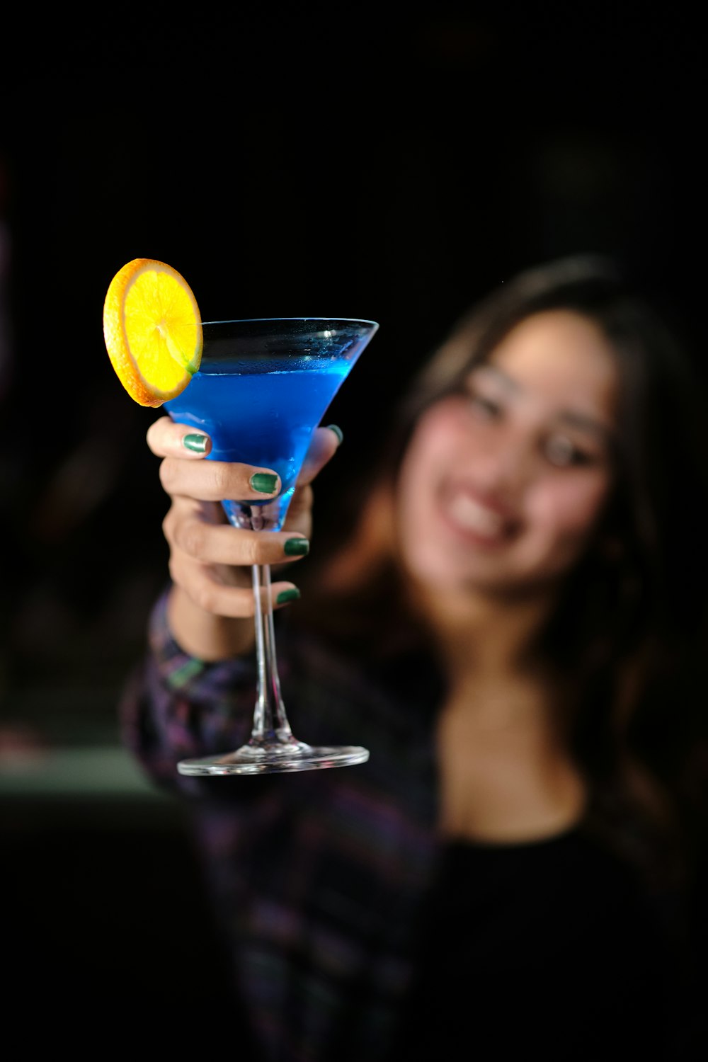 a woman holding a blue cocktail in her hand