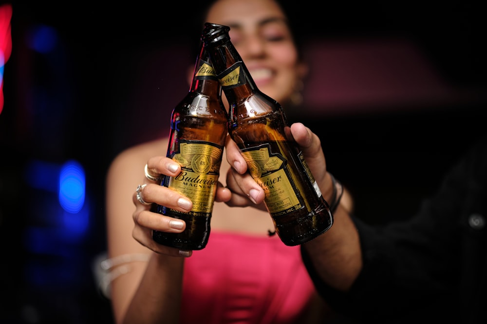 a woman in a pink dress holding two beer bottles