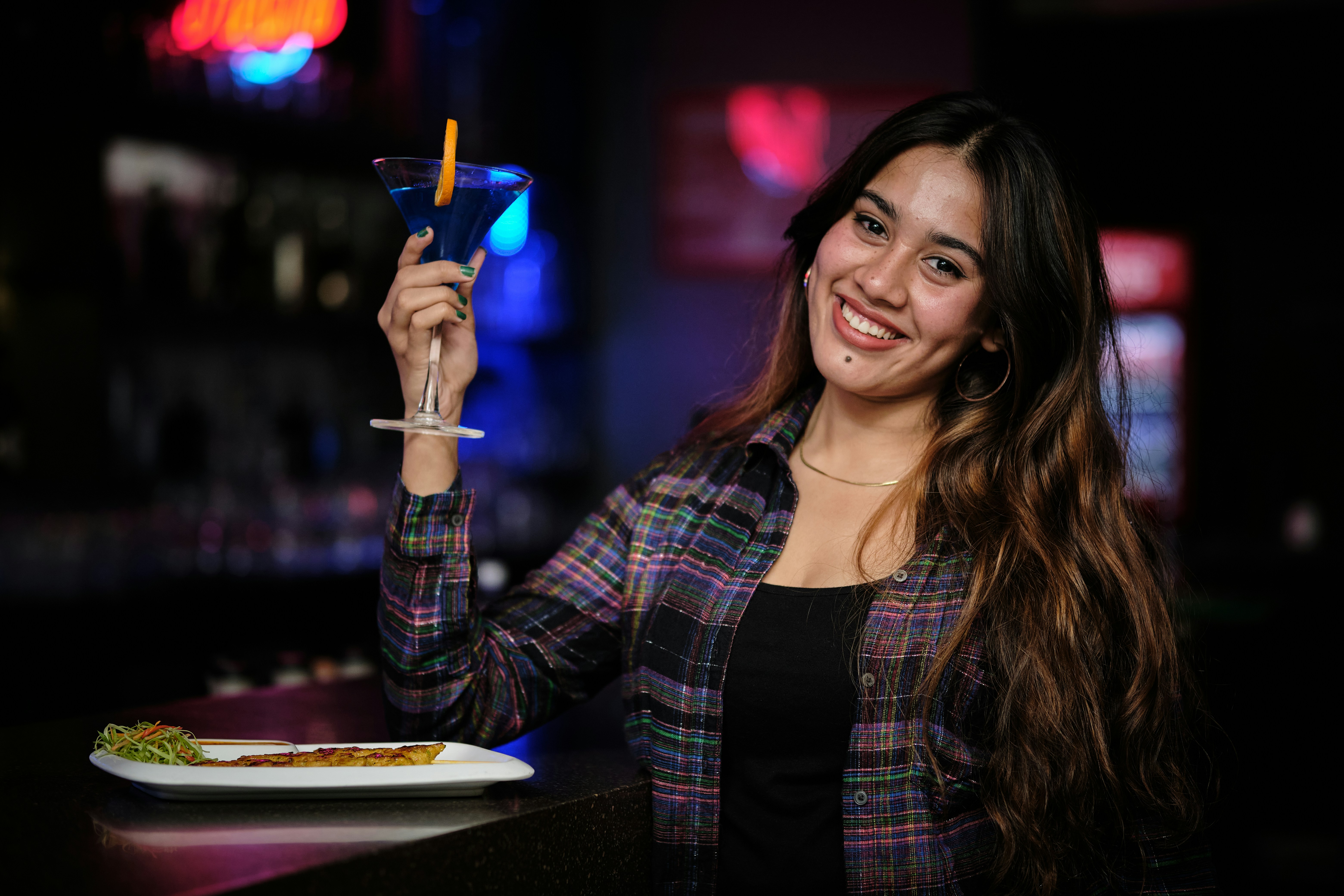 a woman holding up a drink in front of a plate of food