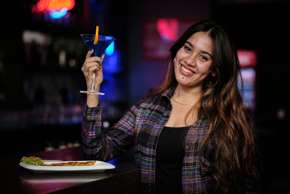 a woman holding up a drink in front of a plate of food