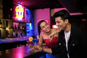 Two wait staff sharing a laugh behind the bar amid bottles and taps