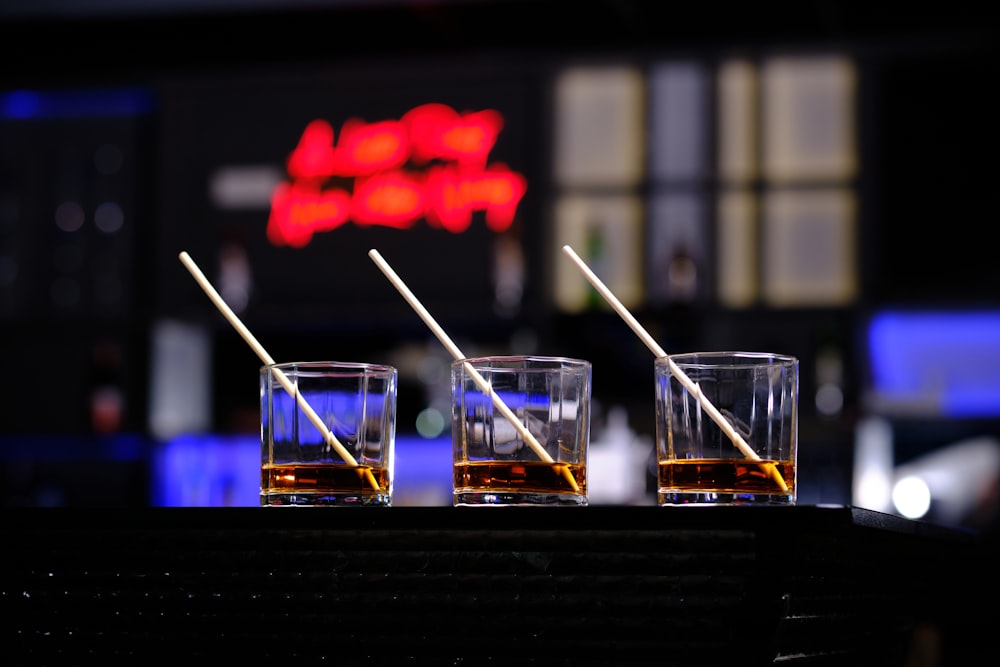 three glasses of whiskey on a bar with a neon sign in the background