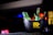 A black ice bucket containing several green beer bottles prominently displaying the brand 'Carlsberg'. The bucket has a yellow text label that reads 'GREAT IS BORN RAW.' and '#Playcraft Gi Copter7'. The background is blurred with colorful lights, suggesting it is possibly taken in a bar or club setting.