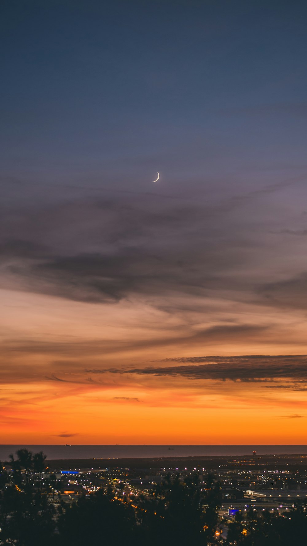a view of a city at sunset with the moon in the distance