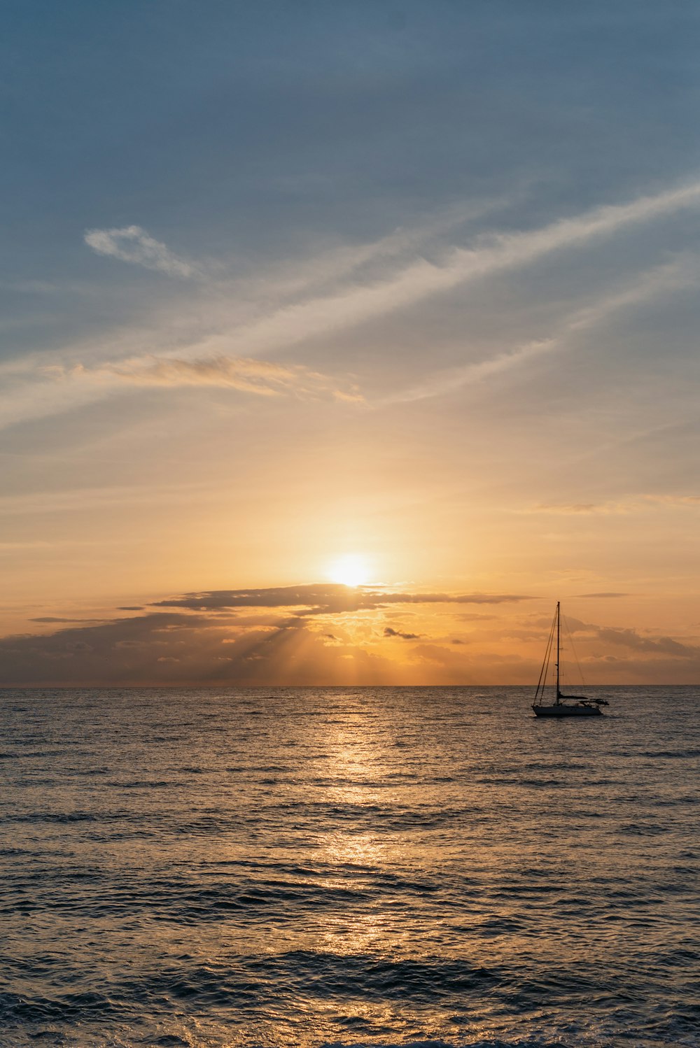the sun is setting over the ocean with a sailboat in the water