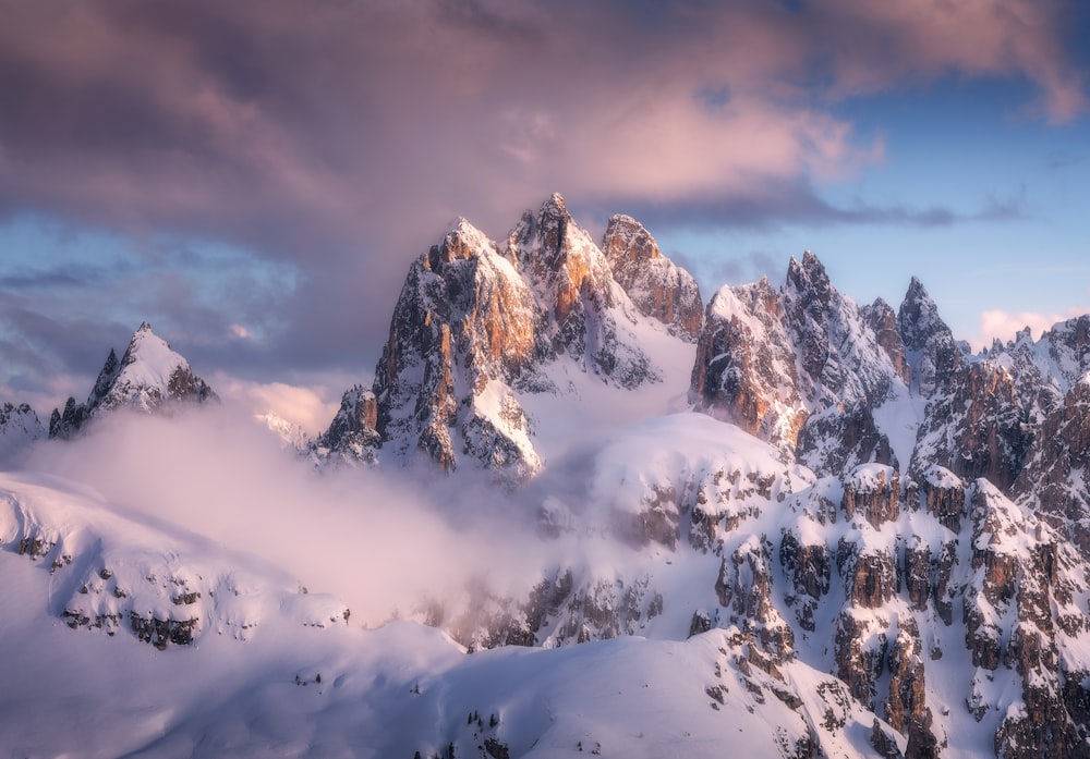 a mountain range covered in snow under a cloudy sky