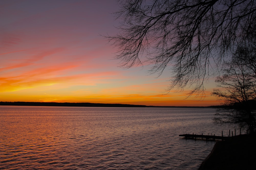 a sunset over a body of water with trees in the foreground