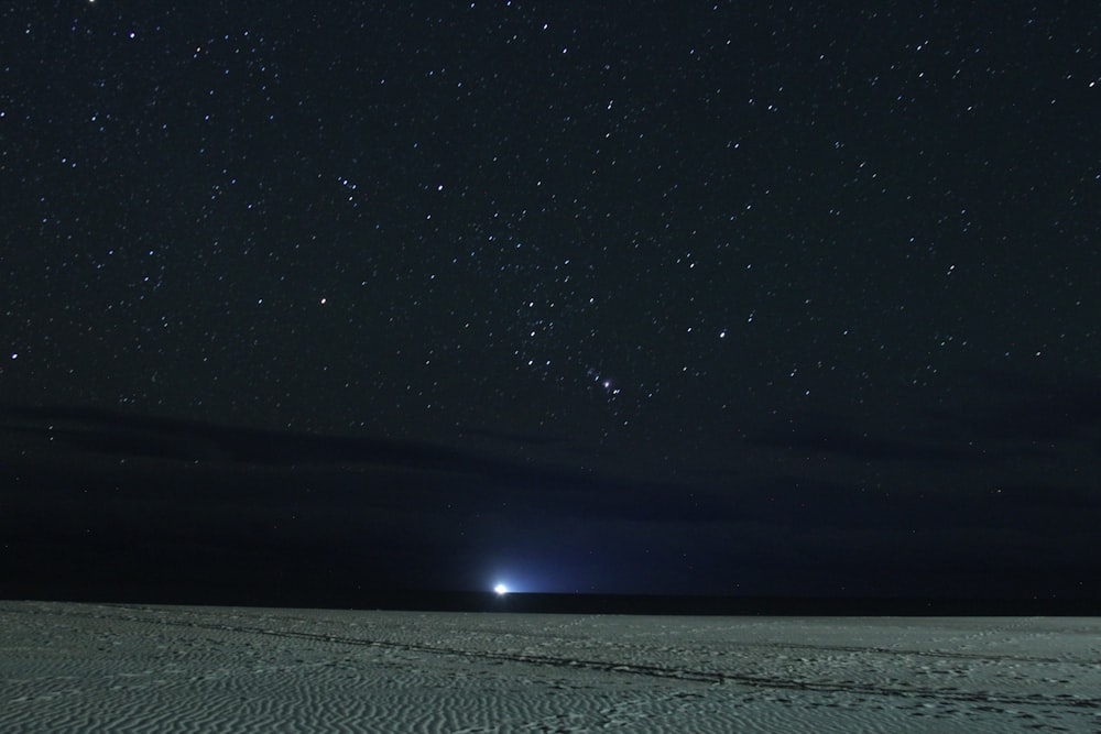 a night sky with stars and a light in the distance