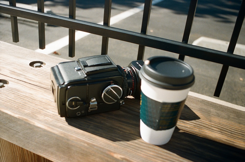 a camera and a coffee cup sitting on a bench
