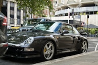 A sleek black manual car parked in front of a vibrant city street in Malang.