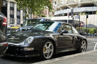 A sleek black manual car parked in front of a vibrant city street in Malang.