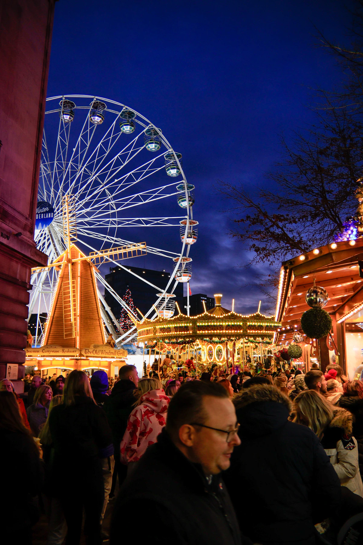 Ferris wheel and carousel lit up above Christmas market stalls at night