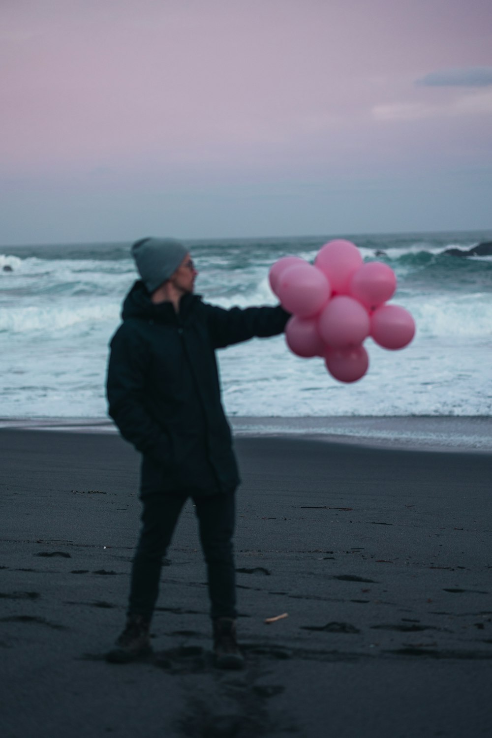 Un hombre parado en una playa sosteniendo un montón de globos rosados