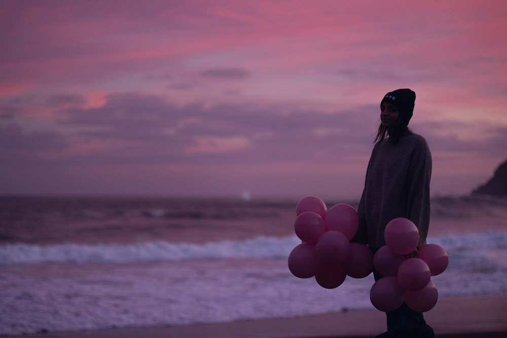 a man standing on a beach holding a bunch of pink balloons