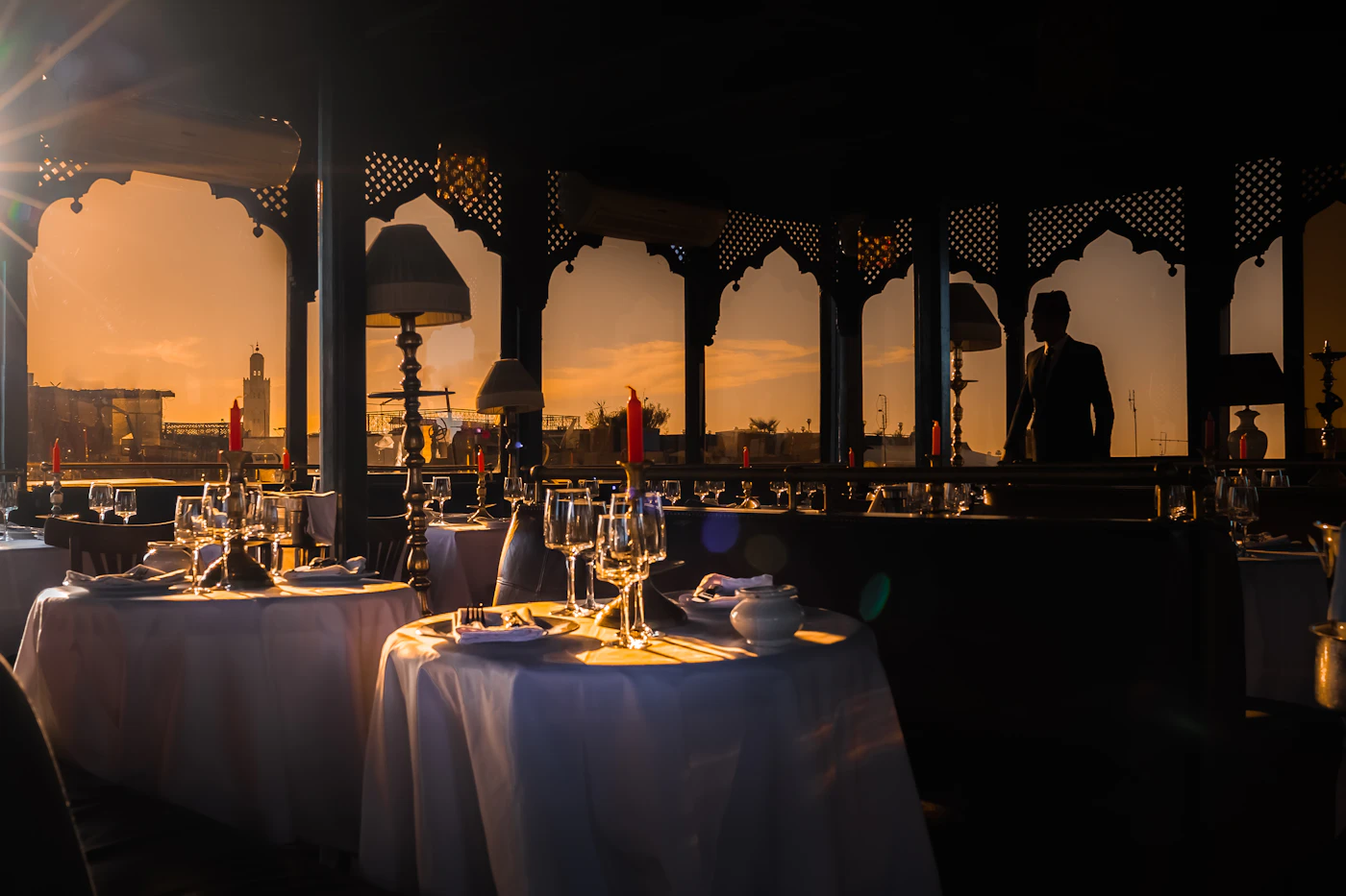 Tables en terrasse rooftop avec verres à vin, vue sur la médina de Marrakech.