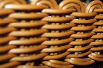 A close-up view of a woven wicker pattern, showcasing a repeating interlocking design with a smooth, polished surface. The image captures the intricate details and texture of the material.
