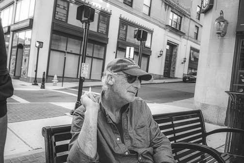 Warm-toned photograph of an elderly man sitting outside a weathered shop in Singapore, sunlight casting long shadows.