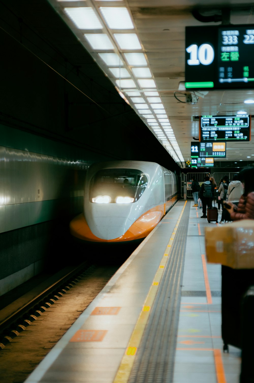 um trem branco e laranja puxando para uma estação de trem