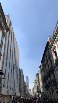 A bustling city street with businesspeople walking past towering office buildings under a clear sky.