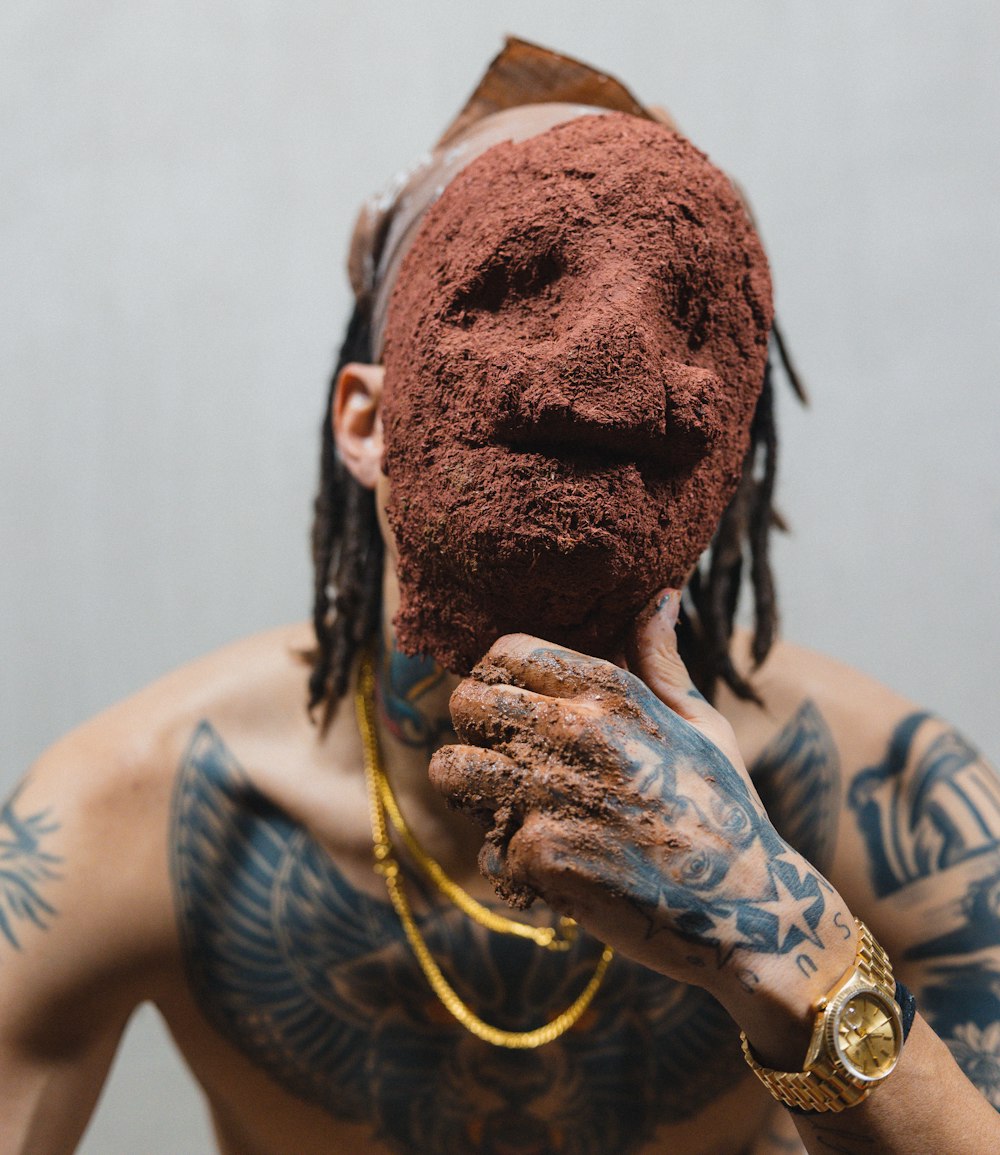 a tattooed man holding a piece of chocolate in front of his face