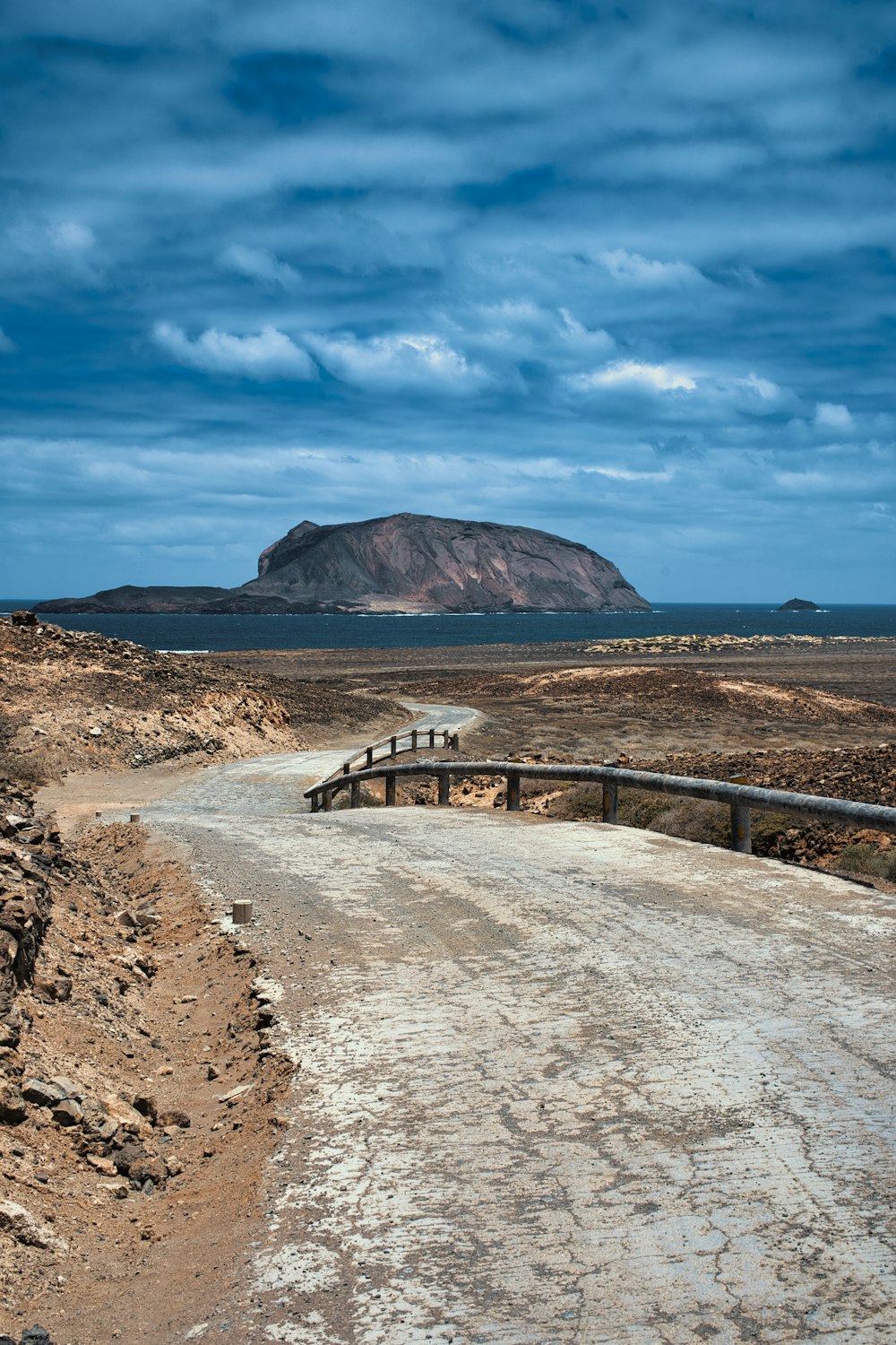a dirt road with a bridge and a mountain in the background