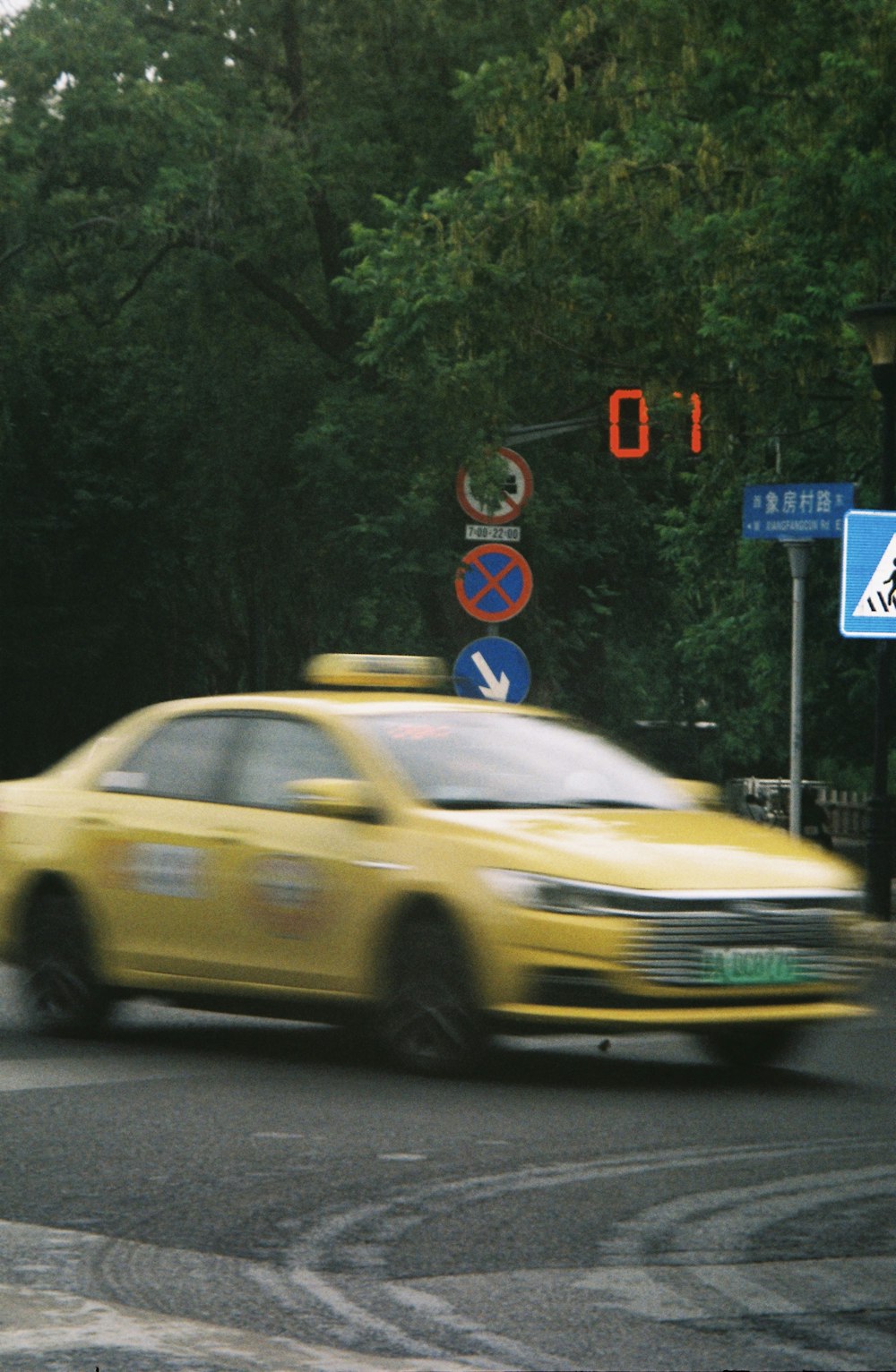 a yellow taxi driving down a street next to a traffic light