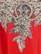 A detailed embroidery pattern featuring intricate floral and leaf motifs adorned with sparkling beads and sequins. The design is set against a vibrant red fabric background, showcasing a blend of gold and black hues in the embellishments.