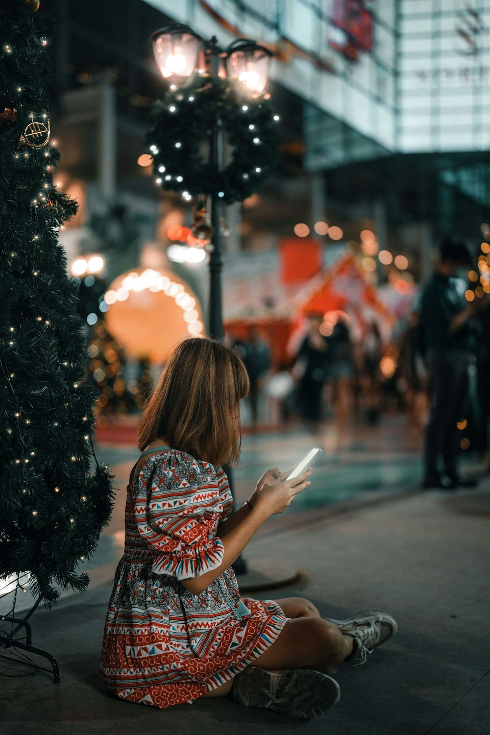 a woman sitting on the ground next to a christmas tree