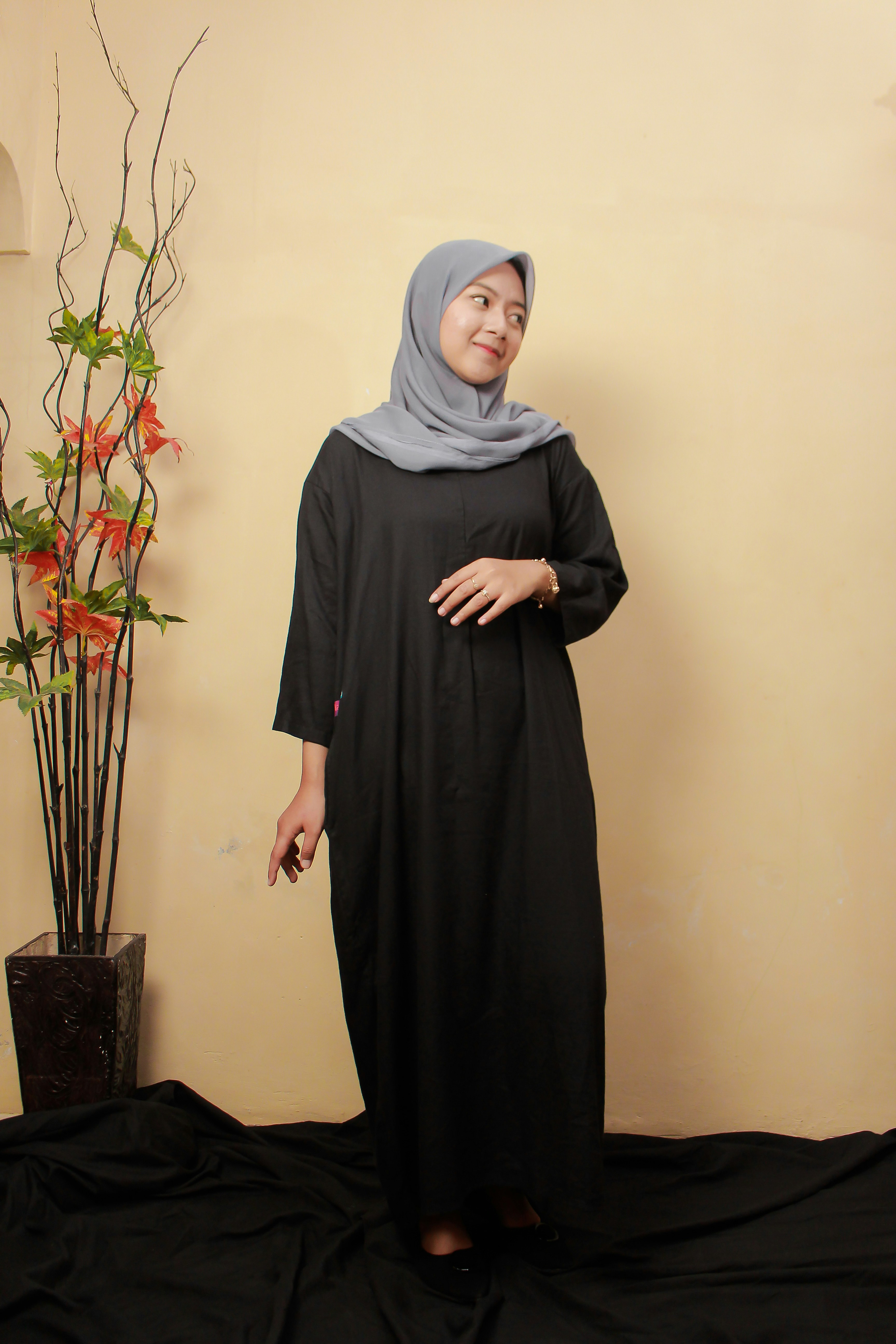 a woman in a black dress standing next to a plant