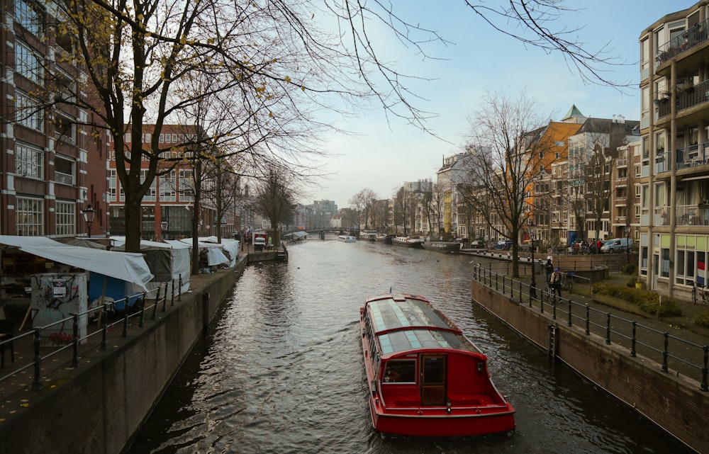 a red boat floating down a river next to tall buildings