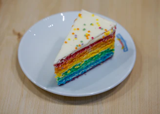 A colorful rainbow layer cake sliced to reveal its bright, multi-colored layers.