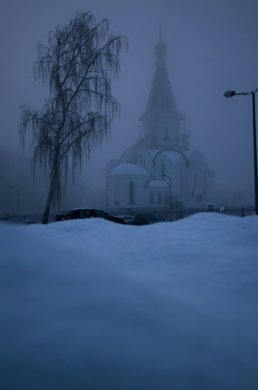a church in the snow with a tree in the foreground