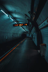 a subway station with a subway sign hanging from the ceiling