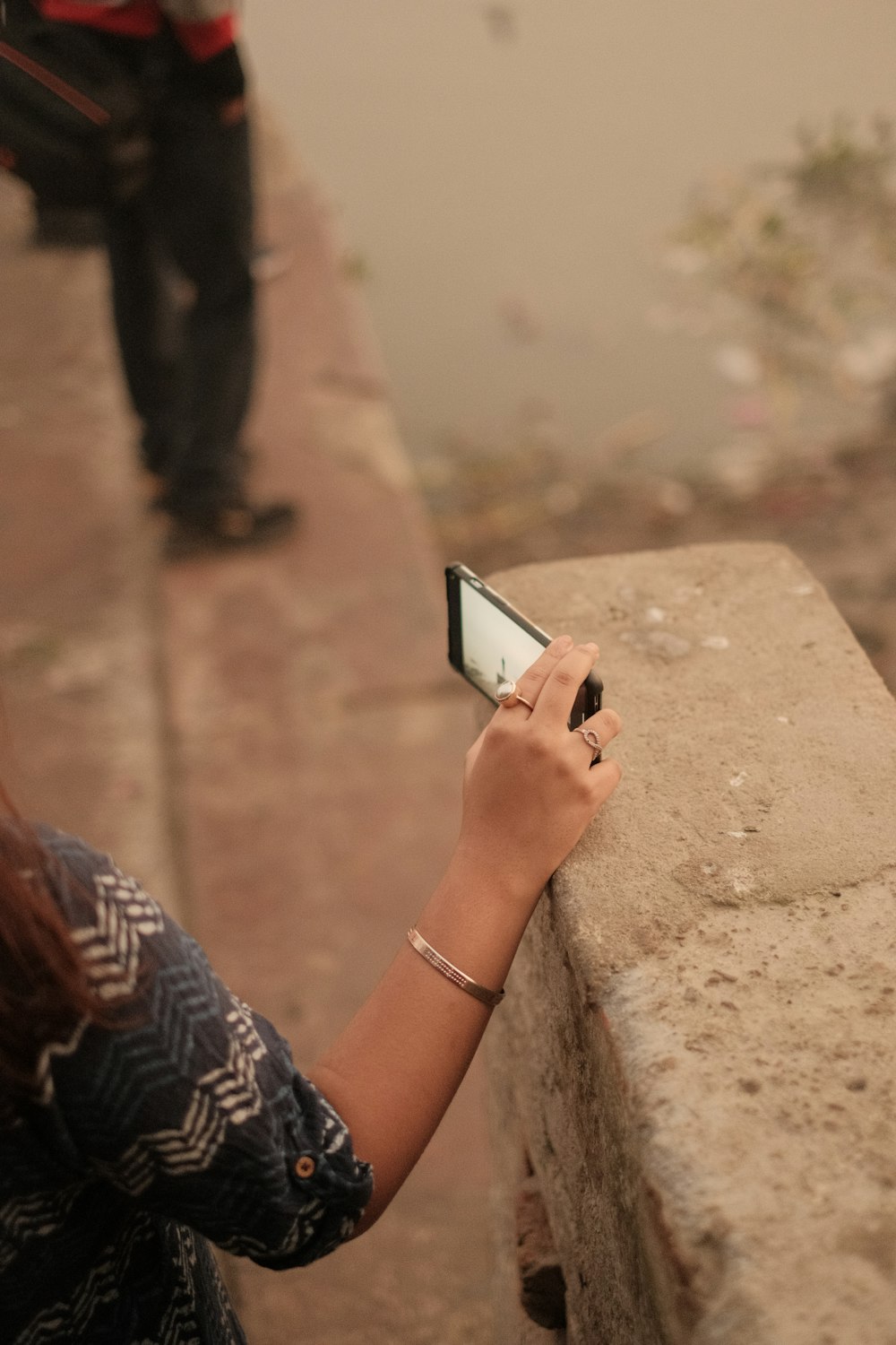 a woman holding a cell phone next to a stone wall