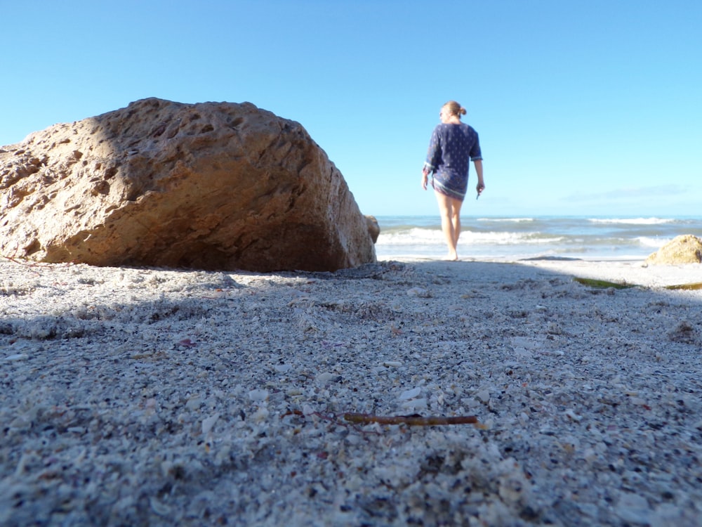 a person walking on a beach next to a large rock