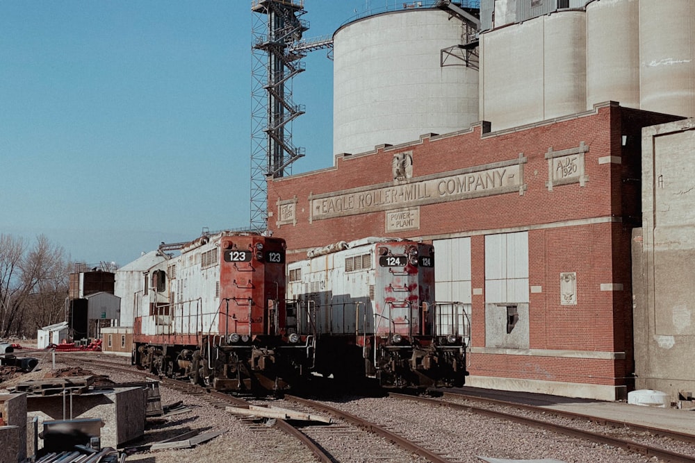 two trains on tracks near a brick building