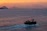 A serene boat gliding through the calm waters of Kotor Bay at sunset.