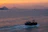 A serene boat gliding through the calm waters of Kotor Bay at sunset.