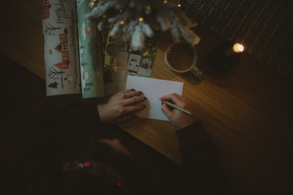 a person writing on a piece of paper next to a christmas tree