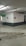 A concrete parking garage corner with visible structural elements, featuring directional exit signs on the walls. The environment appears slightly worn with visible moisture on the ground and overhead lighting. Pipes and conduits are attached to the ceiling.